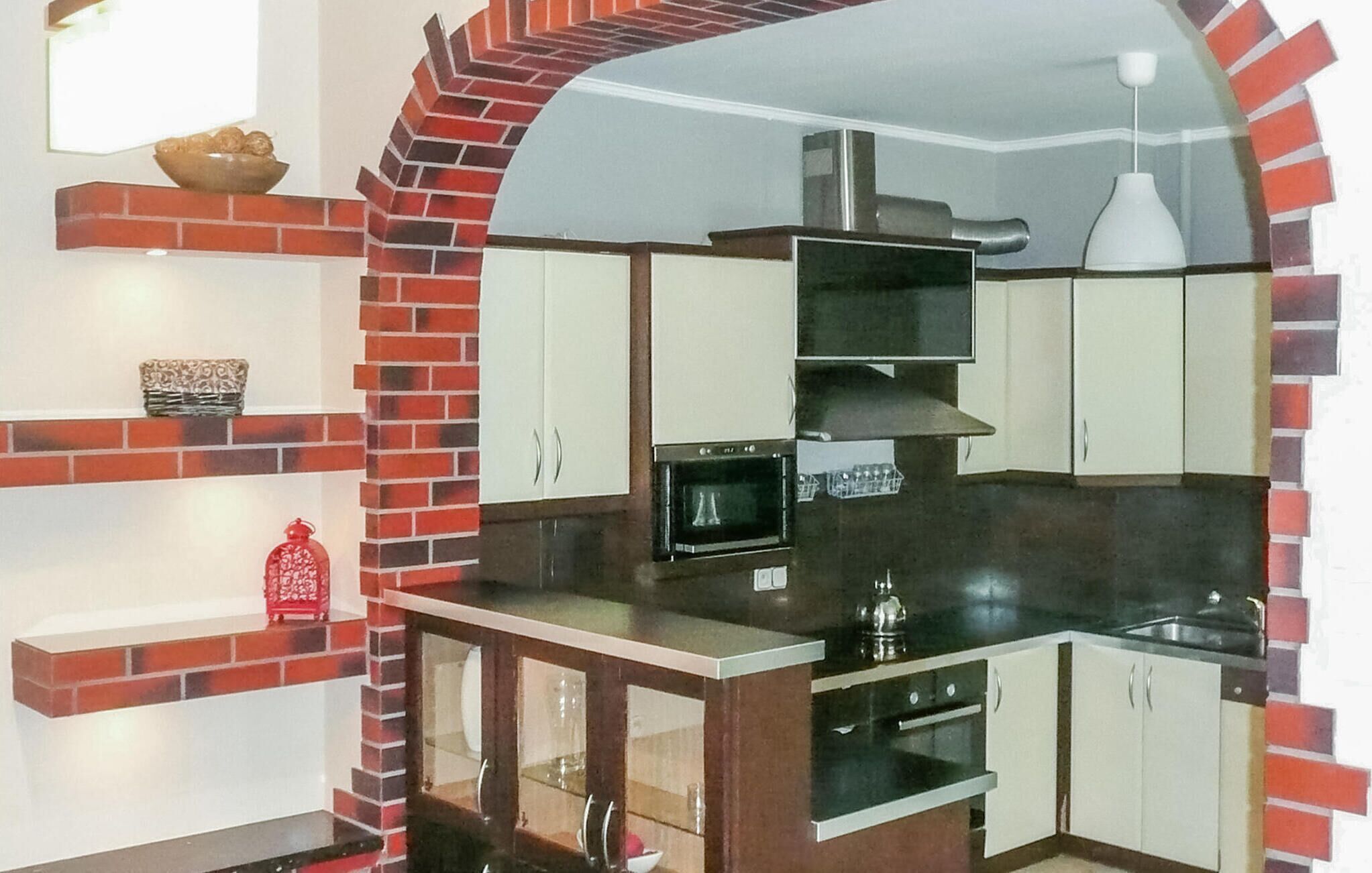 A compact kitchen with a brick arch, white cabinets, and a black countertop.