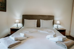 A neatly made bed with white linens and towels, two bedside lamps, and a brown upholstered headboard.