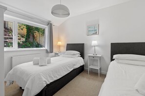 A modern bedroom with a large bed, bedside tables, a lamp, and a view of greenery through a window. - Am Byth - Spectacular Sea Views and Hot Tub (Saundersfoot)