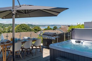 An outdoor patio with a table set for dining, a grill, and a hot tub. - Am Byth - Spectacular Sea Views and Hot Tub (Saundersfoot)