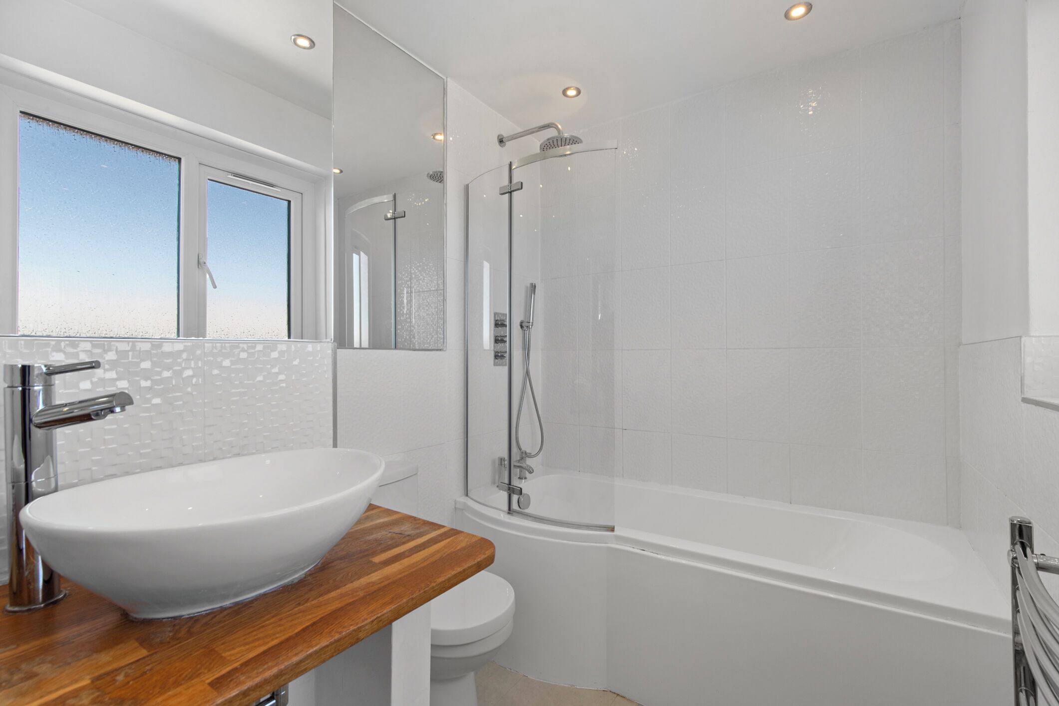 A modern bathroom with a large white sink, a wooden countertop, a toilet, and a glass-enclosed shower area.