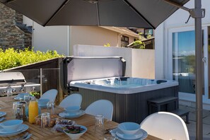 An outdoor dining area with a hot tub, barbecue grill, and a table set for a meal. - Am Byth - Spectacular Sea Views and Hot Tub (Saundersfoot)