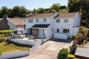 A two-story house with a patio area, a small deck, and a staircase leading to the upper floor. - Am Byth - Spectacular Sea Views and Hot Tub (Saundersfoot)
