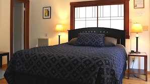 Ein ordentlich bezogenes Bett mit einem gemusterten Überwurf, zwei Nachttische mit Lampen, ein Fenster mit Blick und ein gerahmtes Zertifikat an der Wand.