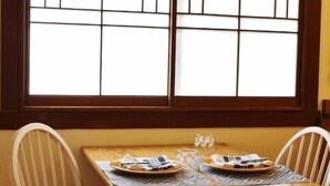 Ein Esstisch mit zwei Stühlen, ein Fenster mit Jalousien und ein kleiner Tisch mit Glas und Teller.