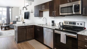 A modern kitchen with dark cabinets, stainless steel appliances, and a granite countertop. - Studio King Suite w/ Kitchen | 200 (Asheville)