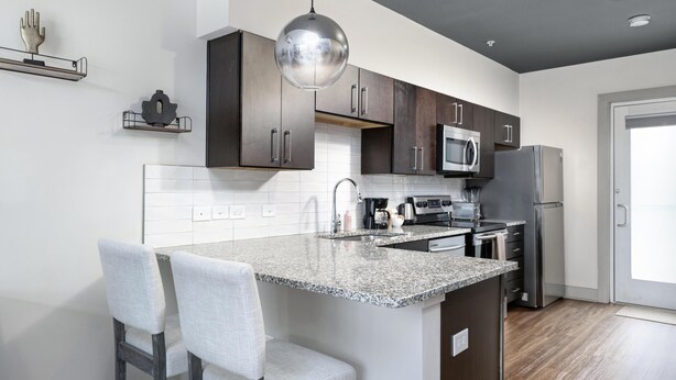 A modern kitchen with dark wooden cabinets, a granite countertop, stainless steel appliances, and a pendant light. - Studio King Suite w/ Kitchen | 200 (Asheville)