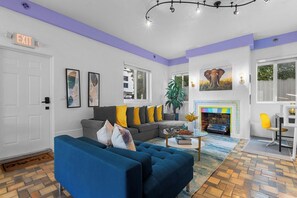 A living room with a blue sofa, a gray couch with yellow pillows, a fireplace, and a large elephant painting on the wall.