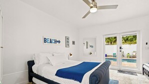Ein Schlafzimmer mit Bett, Deckenventilator, Blick auf einen Pool und einer Tür zum Außenbereich.