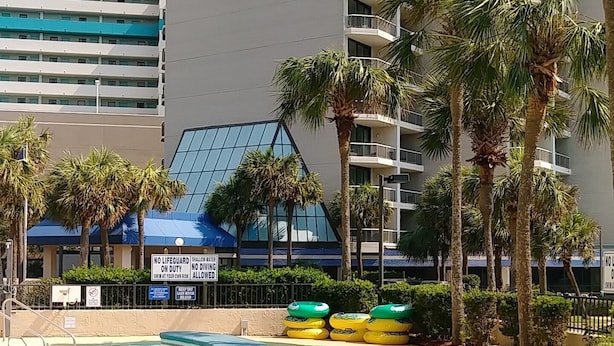 A hotel with a pool area, palm trees, and a sign indicating no lifeguard on duty. - Angle Oceanfront Family Suite at Resort + Official On-Site Rental Privileges (Myrtle Beach)