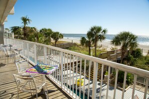A balcony with a view of the beach, clear sky, and palm trees.