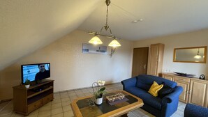 Ein Wohnzimmer mit Fernseher, Sofa, Couchtisch und einer Deckenleuchte.