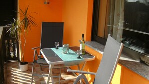 Eine Terrasse im Freien mit Tisch, Stühlen, einer Topfpflanze und einer Weinflasche.