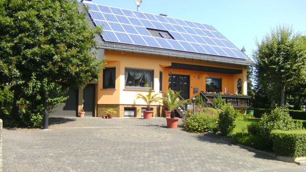 Ein Haus mit Solardach, befestigter Auffahrt und Blumentöpfen.
