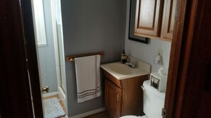 Un baño pequeño con un lavamanos blanco, armarios de madera y una toalla colgada en un perchero.
