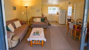 Un espace de vie compact comprenant un ensemble canapé, une table à manger avec des chaises, un coin cuisine et une petite table avec un livre.