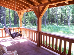 A wooden deck with a swing and a bench, overlooking a forested area.