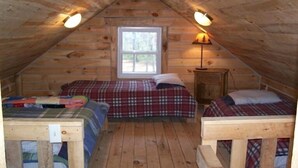 A cozy attic bedroom with two beds, a window, and a lamp. - Private Amish Log Cabin Getaway (Black River Falls)