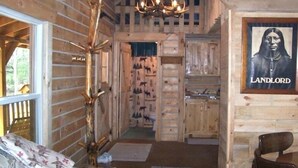 A log cabin interior with a wooden staircase, a chandelier, a framed picture labeled "LANDLORD," and a dining area with a table and chairs. - Private Amish Log Cabin Getaway (Black River Falls)
