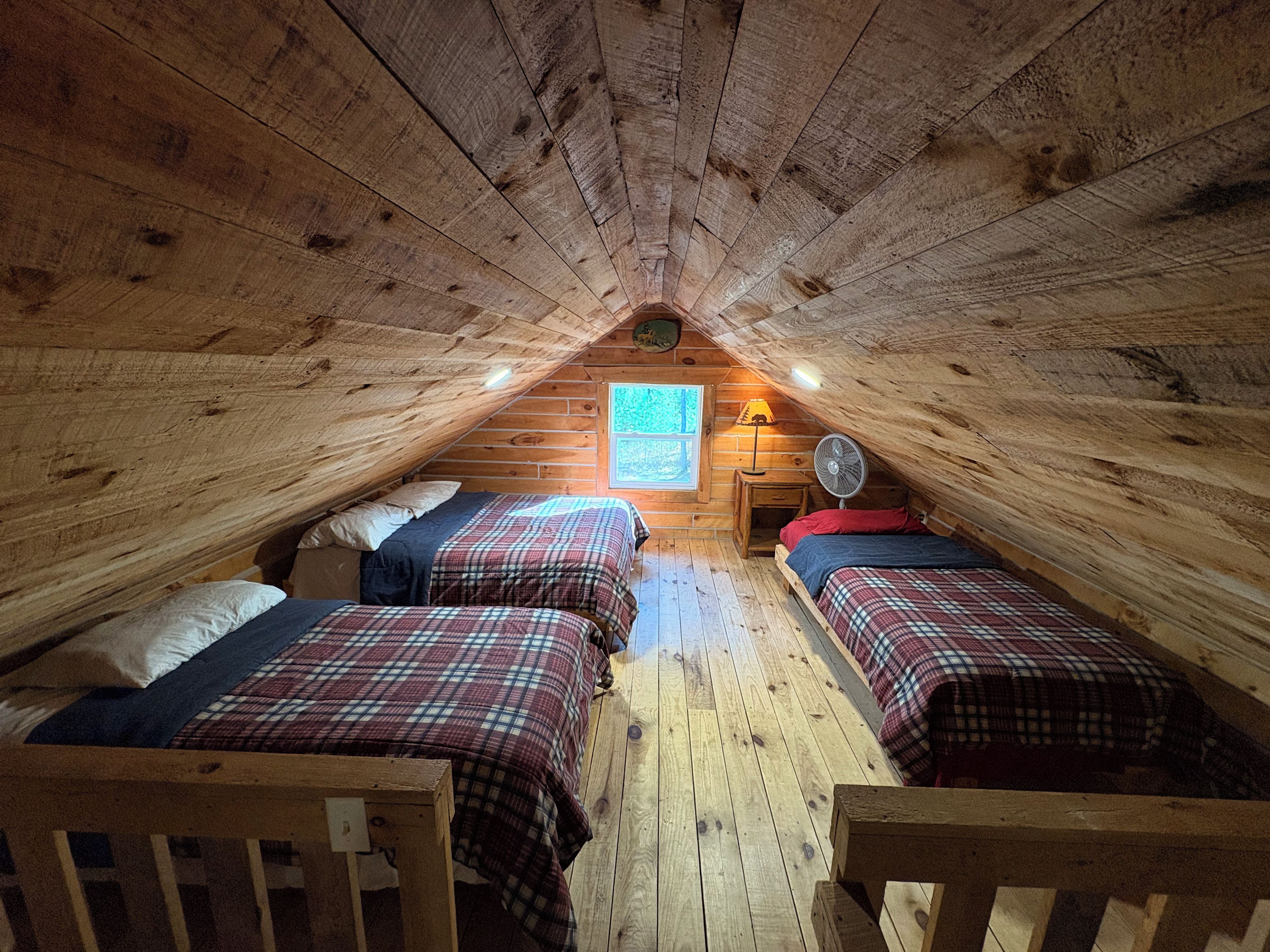 A cozy attic bedroom with two beds, a fan, and a window with a map.