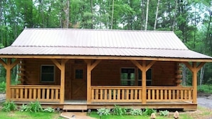 A wooden cabin with a porch, a front door, and a small front yard with a pathway and potted plants. - Private Amish Log Cabin Getaway (Black River Falls)