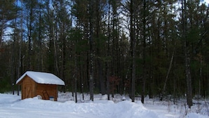A wooden cabin with a snow-covered roof, surrounded by a forest and a snow-covered ground. - Private Amish Log Cabin Getaway (Black River Falls)