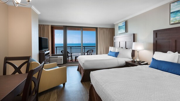 A hotel room with two beds, a TV, a dining area, and a balcony with a view of the ocean. - Oceanfront Double Efficiency w/ View + Official On-Site Rental Privileges (Myrtle Beach)