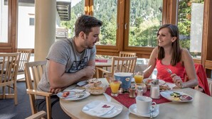 A couple dining at a table with a mountain view, breakfast plates, and a coffee cup. - Hotel Kärntnerhof Mallnitz (Mallnitz)