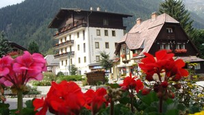 A hotel with a traditional Alpine architectural style, featuring a balcony with flowers, set against a backdrop of mountains. - Hotel Kärntnerhof Mallnitz (Mallnitz)