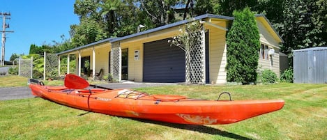 A single-story building with a garage, a covered porch, and a red kayak on the grass.