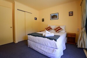 Une chambre d’hôtel avec un lit, une table de chevet, une porte et un mur orné de deux tableaux.