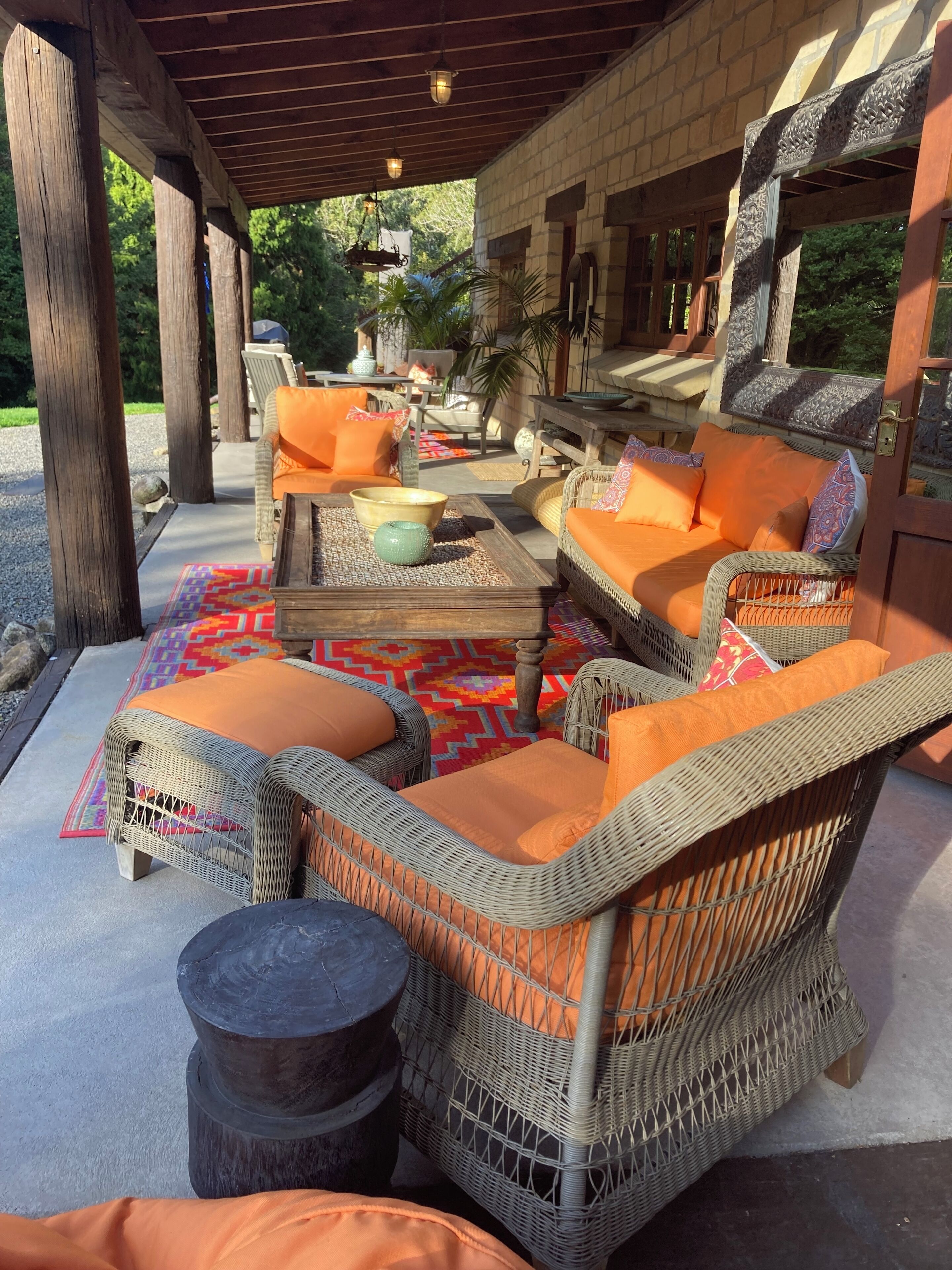 An outdoor seating area with wicker furniture and orange cushions, a wooden table, and a patterned rug.