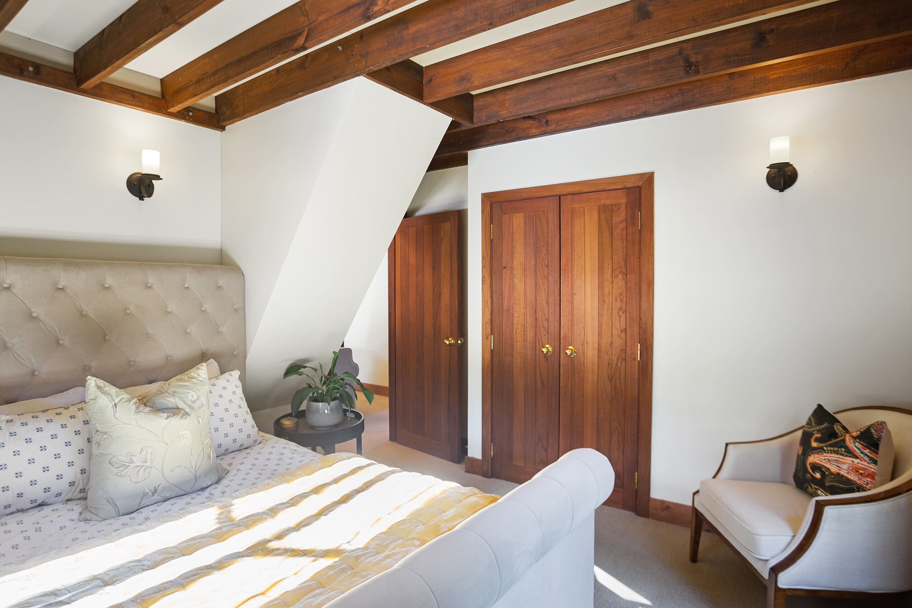 Un dormitorio con una cama grande, una silla, armario de madera y una planta en maceta.