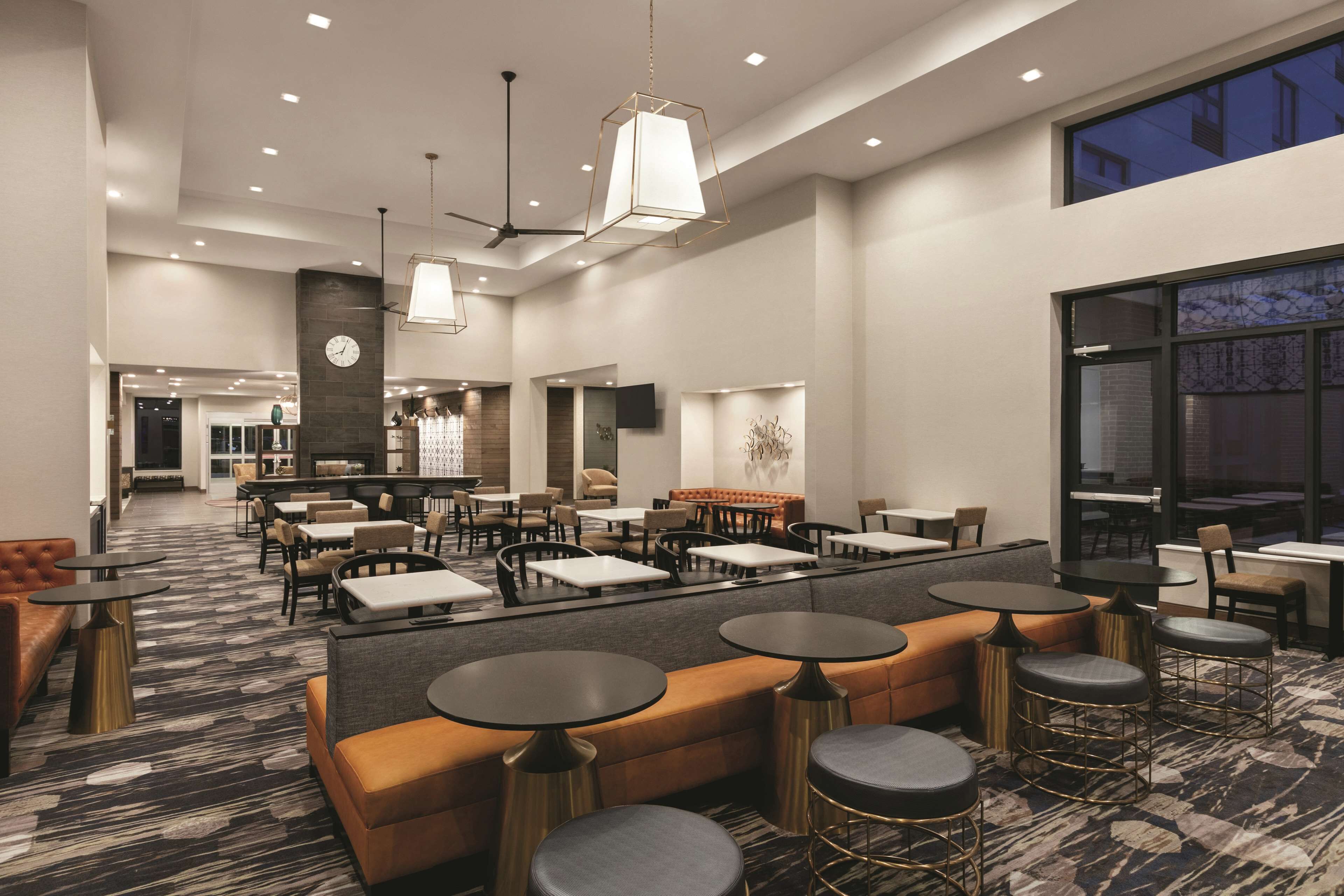 Eine großzügige Hotelhalle mit mehreren Sitzbereichen, darunter Sofas und runden Tischen. Deckenventilatoren und Pendelleuchten sorgen für Beleuchtung.