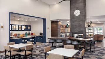 Un moderno vestíbulo de hotel con un bar central, área de estar y un reloj en la pared.