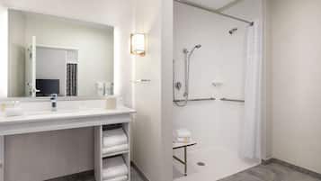 A modern bathroom with a large mirror, white sink, and a walk-in shower.