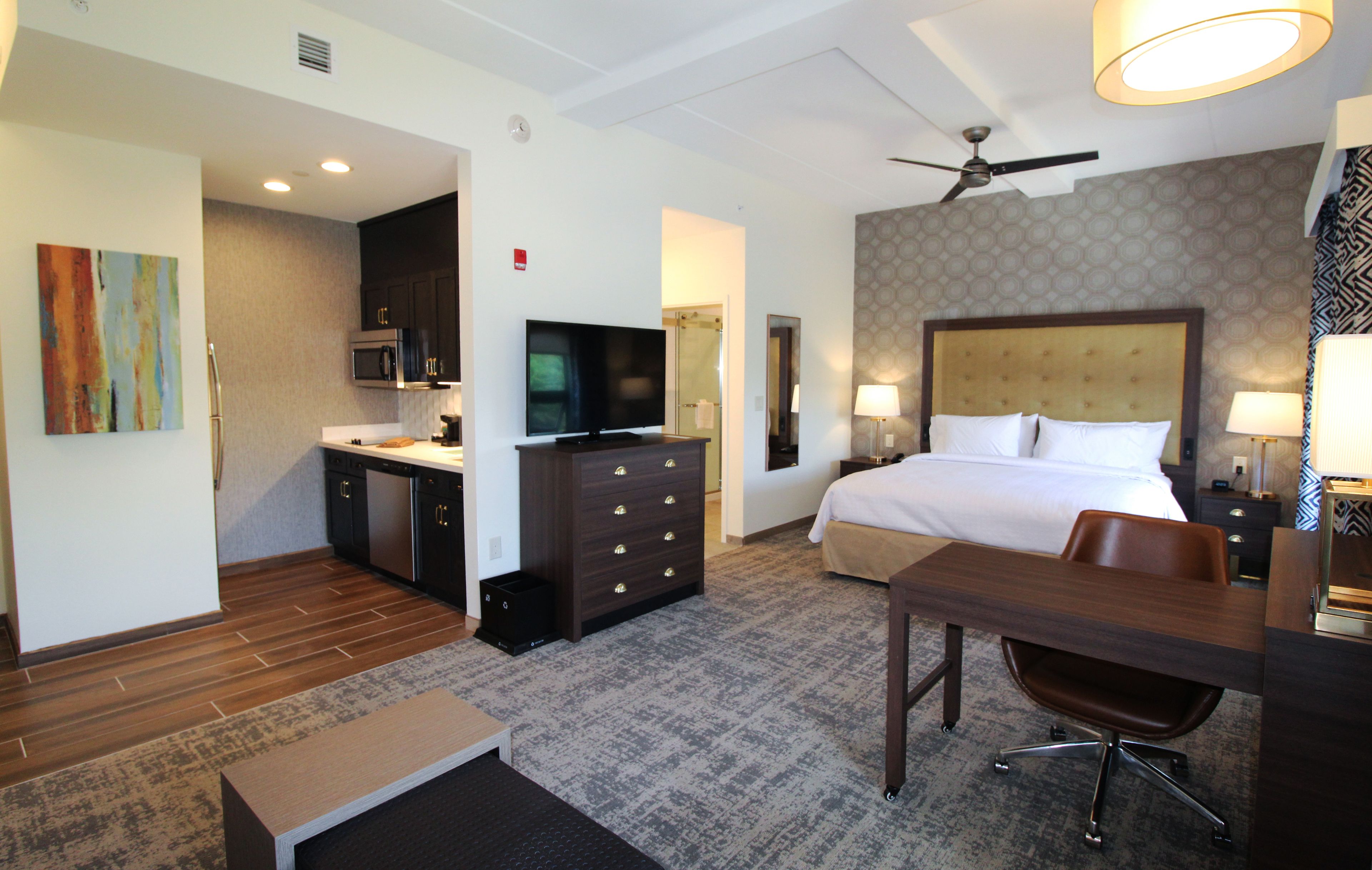 A hotel room with a bed, desk, chair, television, and kitchenette.