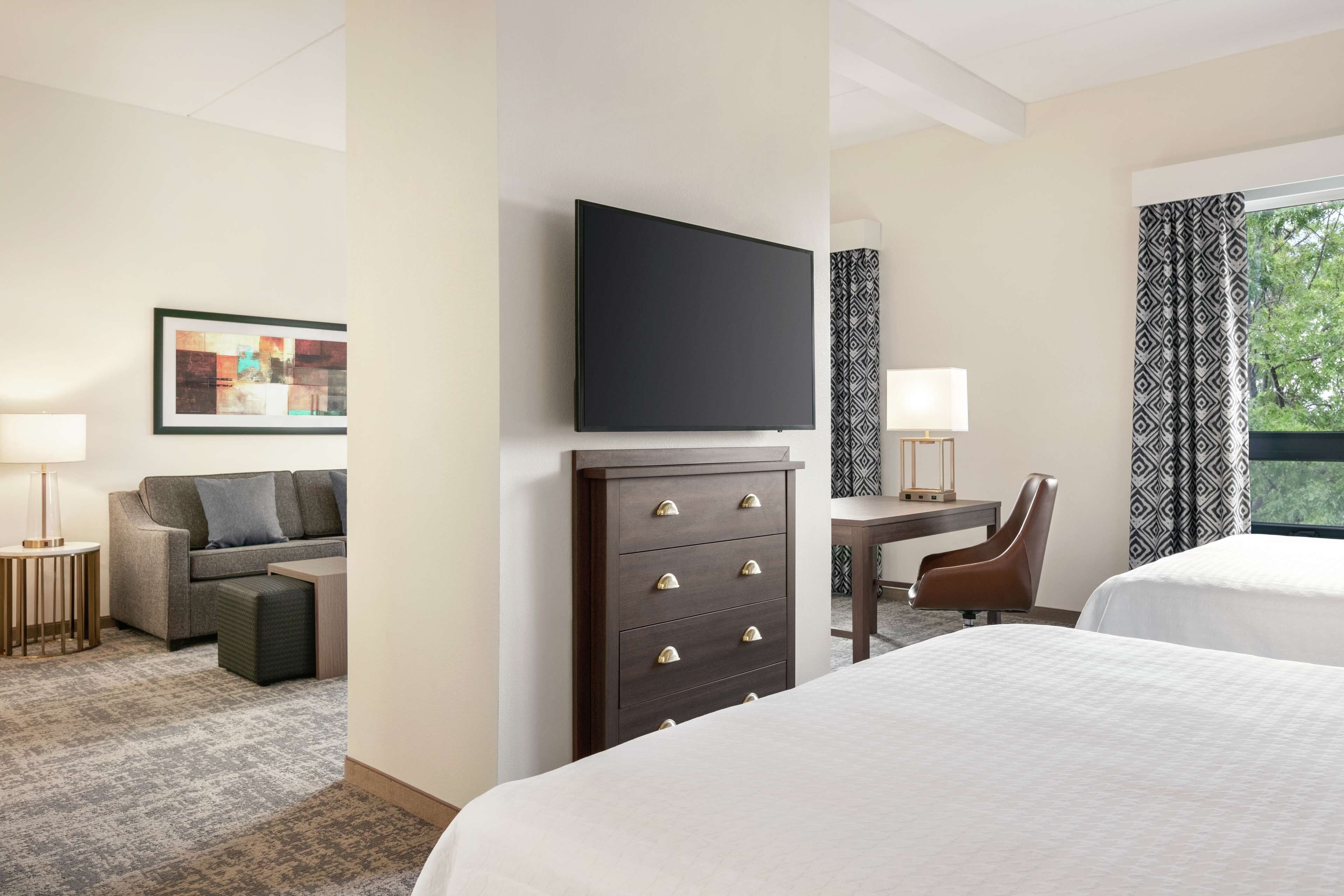A hotel room with a bed, a desk, a chair, a TV, a dresser, and a sofa.