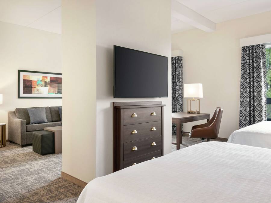 A hotel room with a bed, a desk, a chair, a TV, a dresser, and a sofa.