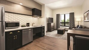 A modern kitchen with a microwave, stove, and dishwasher. There is a dining area with a table and chairs, and a sofa in the living room. - Homewood Suites by Hilton Horsham Willow Grove (Horsham)