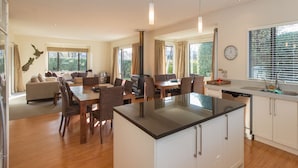 Une cuisine moderne dotée d’un îlot central, d’un coin repas avec une table et des chaises en bois, et d’un salon avec un canapé et une cheminée.