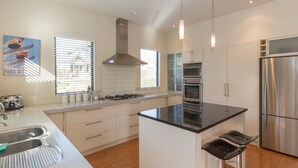 Une cuisine moderne avec des meubles blancs, des appareils en acier inoxydable, un îlot central et des tabourets de bar.