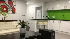 Une cuisine moderne avec des meubles blancs, un pare-feu vert et un plan de travail noir. On y trouve un canapé blanc et une table noire sur laquelle est posée une plante en pot.