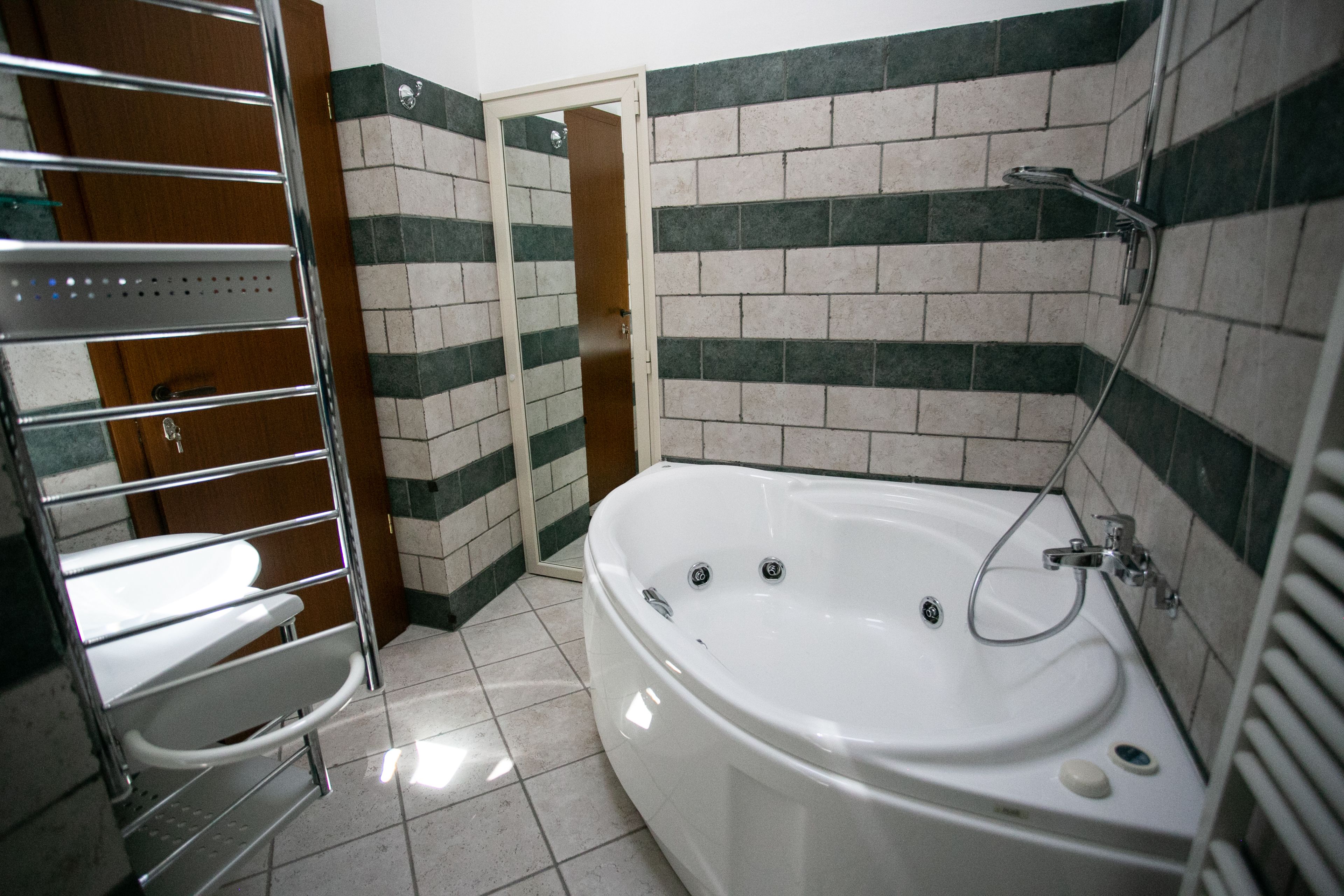 A bathroom with a white bathtub, a shower, and a toilet. The walls are tiled with a green and white pattern.