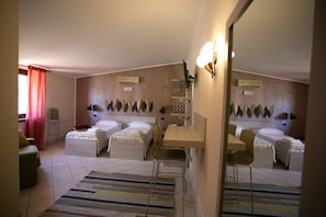 A hotel room with two beds, a desk, a chair, a small table, a mirror, and a window with curtains. - B&B Trepo (Tropea)