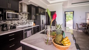 A modern kitchen with dark cabinets, a microwave, and a large island with a bowl of fruit and a vase. - Exclusive Pool Oasis: Stunning Views! Sleeps 8, Nature's Seclusion (Puntarenas)