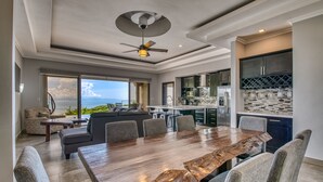 A spacious living area with a large wooden dining table, comfortable seating, a ceiling fan, and a view of the ocean. - Exclusive Pool Oasis: Stunning Views! Sleeps 8, Nature's Seclusion (Puntarenas)