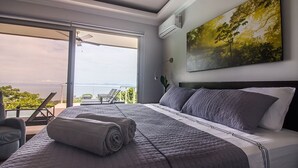 A bedroom with a large bed, a view of the outdoors, and a painting on the wall. - Exclusive Pool Oasis: Stunning Views! Sleeps 8, Nature's Seclusion (Puntarenas)