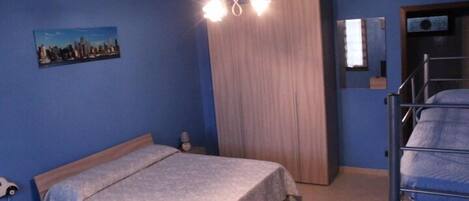 Un dormitorio con cama, armario, espejo y un cuadro de paisaje urbano en la pared.