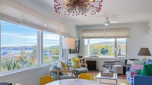 A modern living room with a large window, a dining area, and a ceiling fan.